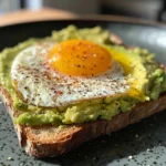 Avocado toast topped with two fried eggs and cherry tomatoes.
