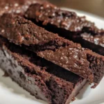 Slices of fudgy chocolate zucchini bread topped with chocolate chips, served on a light-blue oval plate.