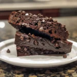 A loaf of insanely moist vegan double chocolate zucchini bread on a white platter, with a slice cut out.